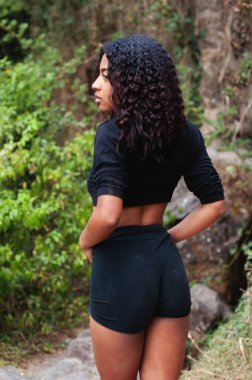 Şık, modaya uygun genç bir kadın, güzel doğal buklelerini sergileyerek, güvenli bir şekilde dışarıda poz veriyor.