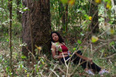 Genç bir kadın yemyeşil yemyeşil bir ağaçla çevrili, huzur ve sükuneti somutlaştıran muhteşem bir ağaçla rahatlar.