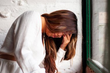 Düşünceli bir kadın pencerenin kenarında zarif bir şekilde durur, sıcak ve davetkar doğal ışıkta derin duygular taşır.