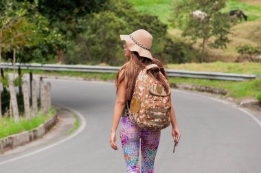 Şık bir sırt çantası olan genç bir kadın verimli, canlı yeşilliklerle çevrili dolambaçlı bir yolda rahatça yürüyor.