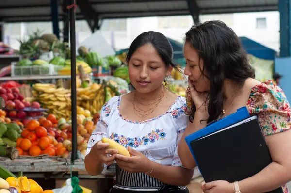 İki kadın canlı bir pazarda renkli ve taze meyveleri inceleyerek yerel kültür ve toplumsal bağlılık sergilediler.