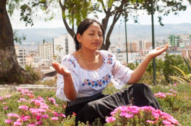 Sakin bir kadın dingin çiçekler ve çarpıcı şehir manzarası arasında sakince meditasyon yapar.