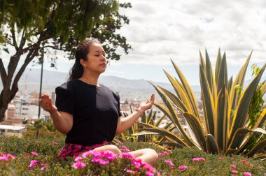 Açık havada meditasyon yapan bir kadın, canlı doğaya dalmış, derin sükunet ve farkındalığı somutlaştırıyor.