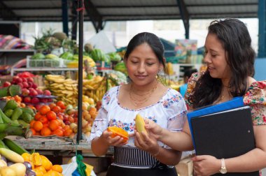 İki kadın canlı yerel bir pazarda çeşitli taze ve egzotik meyveleri zevkle keşfedip yerel tarımları sergiliyor.