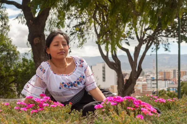 Canlı geleneksel giysiler içinde genç bir kadın doğada çiçek açan çiçekler arasında huzurlu bir anın tadını çıkarıyor..