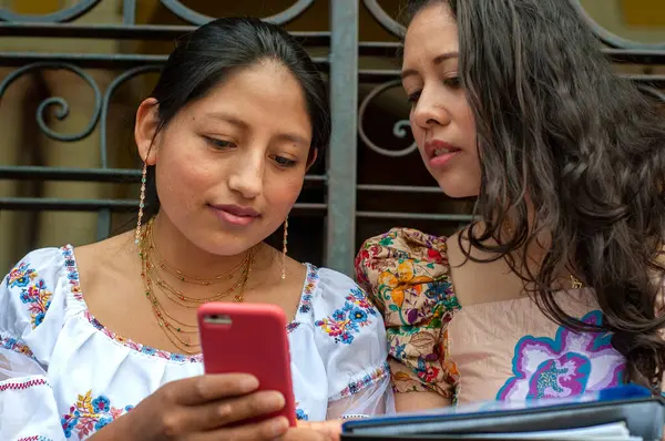 İki kadın bir cep telefonunu yakından inceliyor, kültürel bağlamda etkileşim ve teknoloji sergiliyor.