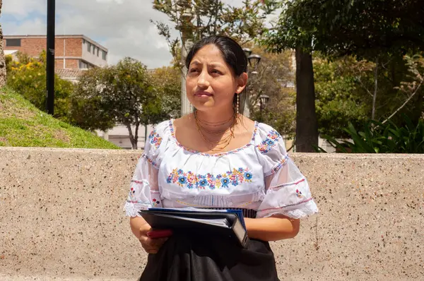 Bir kadın geleneksel giysiler içinde şık bir şekilde giyinir ve elinde bir tablet taşır.