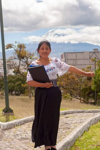 Geleneksel giyinmiş bir kadın, kültürel mirası somutlaştıran manzaralı bir dağ zeminine karşı duruyor..