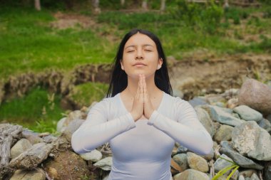 Huzurlu bir kadın etrafındaki sakin ve doğal bir çevrede derin bir meditasyona dalmış.
