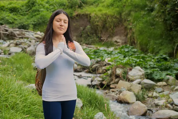 Genç bir kadın, yeşilliklerle çevrili bir derede meditasyon yapıyor, doğayı kucaklıyor, güzelliği kucaklıyor ve huzur arıyor.