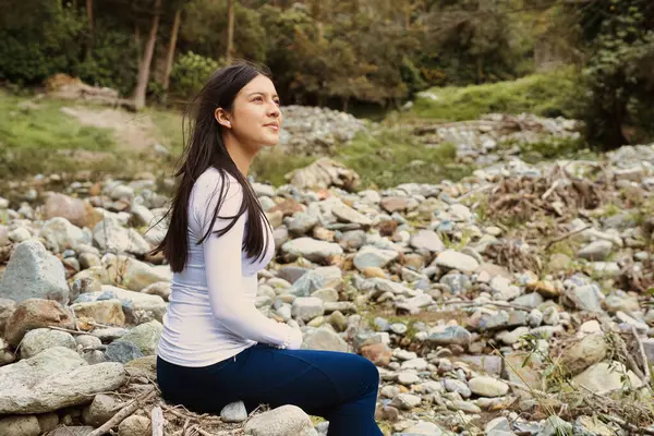 Genç bir kadın, sakin bir doğal ortamda kayaların arasında huzur içinde oturur ve yalnızlığını tamamen benimser.