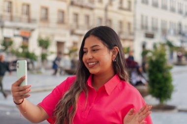Neşeli genç bir kadın canlı bir şehir meydanında selfie çekiyor, neşe ve modern yaşam tarzı sergiliyor..