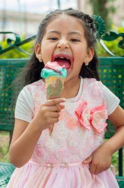 Genç bir kız dışarıda oynarken mutlu bir şekilde gülüyor ve renkli ve canlı bir dondurma külahının tadını çıkarıyor.