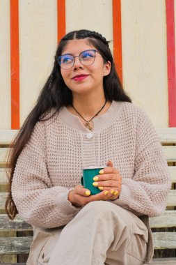 Şık bir kadın içkisini rahat bir süveter ve şık gözlüklerle rahatlar, canlı bir atmosferin tadını çıkarır.