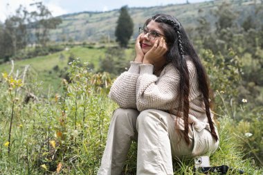 Düşüncelere dalmış genç bir kadın, yemyeşil ve dağlarla çevrili, sükunet ve neşe dolu..