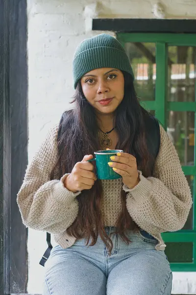 Çevresindeki doğanın güzelliğine dalmış, rahat bir kıyafet giyerek sıcak bir içkinin tadını çıkaran bir kadın.