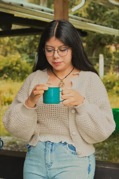 Rahat bir süveter giyen bir kadın güzel bir açık hava ortamında sıcak bir fincan kahvenin tadını çıkarıyor.