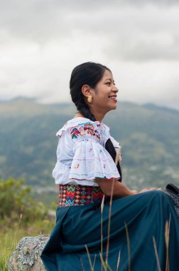 Genç bir kadın, canlı bir manzaraya karşı güzel, geleneksel Ekvador kıyafetleriyle güven içinde poz verir.
