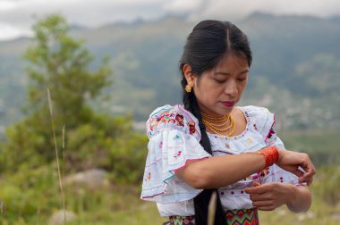Geleneksel giyinmiş yerli bir kadın mücevherlerini manzaralı bir dağ manzarasına göre ayarlıyor.