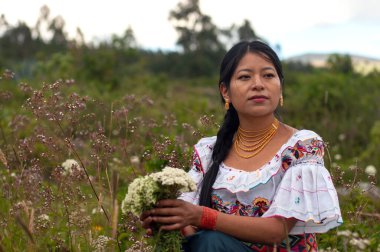 Geleneksel elbiseli bir kadın elinde çiçeklerle doğal çevrede yerli kültürünü sergiliyor..