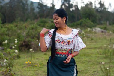 Genç bir kadın zengin kültürünü sevinçle kutlarken canlı geleneksel giysiler giyerek manzaralı bir arka plana çıkıyor.