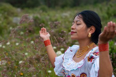 Geleneksel giyinmiş dingin bir kadın yemyeşil bir alanda farkındalık üzerine çalışıyor.