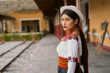 Geleneksel Andean giysileri ve şapka giyen yerli riobamba kadını, ekvatorun zengin kültürel mirasını sergilemek için tren istasyonunda poz veriyor.