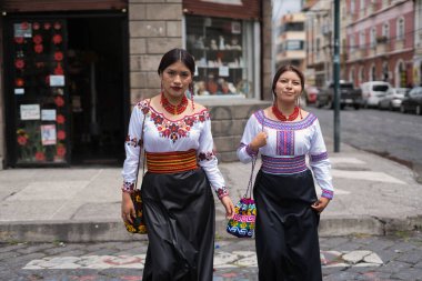 İki kadın, canlı nakış ve desenli geleneksel yerli kıyafetleri giyerek güvenli bir şekilde şehir caddesinde yürüyorlar. Kıyafetleri kültürel mirası ve modern tarz birleşimini ön plana çıkarıyor.