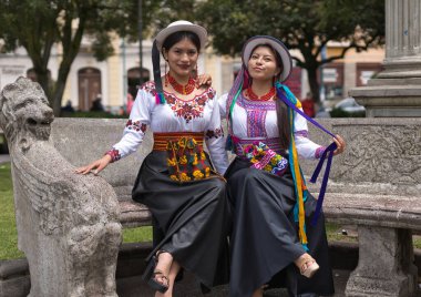 Geleneksel riobamaba kıyafetleri ve şapkalar giyen iki gülümseyen yerli kadın zengin kültür mirasını temsil eden Riobamba, Ekvador 'daki bir parkta taş bir bankta oturuyorlar.