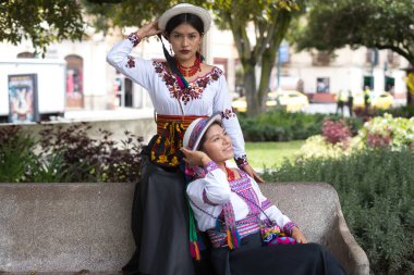 Geleneksel yerli kıyafetli iki kadın bereketli bir şehir parkında bir anın tadını çıkarıyorlar. Renkli kıyafetleri ve özgüvenli ifadeleri yerli modanın güzelliğini ve kültürel zenginliğini vurguluyor.