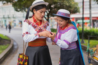 Geleneksel andean kıyafetleri ve şapkalar giyen iki gülümseyen yerli riobamba kadını, ekvador bir şehirde kültür ve teknolojinin karışımını sergileyen bir akıllı telefon kullanıyorlar.