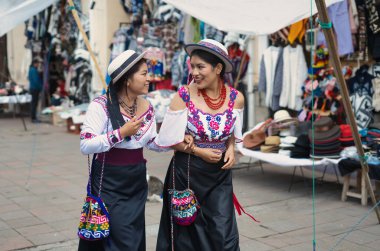 Geleneksel andean kıyafetleri ve şapkalar giyen iki gülümseyen yerli riobamba kadını otavalo 'da tekstil ve giysi satıyorlar.