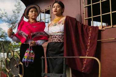 Geleneksel Andean giysileri giyen iki model, canlı renkleri ve kültürlerinin karmaşık tasarımlarını sergileyen eski bir trende poz veriyorlar.