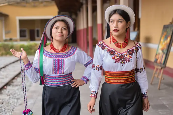 Geleneksel ve dekan işlemeli bluzlar giyen iki gülümseyen yerli riobamba kadını, renkli kemerler ve Ekvador 'daki eski tren istasyonunda yürüyen beyaz şapkalar.