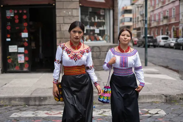 İki kadın, canlı nakış ve desenli geleneksel yerli kıyafetleri giyerek güvenli bir şekilde şehir caddesinde yürüyorlar. Kıyafetleri kültürel mirası ve modern tarz birleşimini ön plana çıkarıyor.