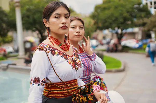 Geleneksel işlemeli bluz ve kolyelerini takmış iki otavalo yerlisi kadın, ekvatorun otavalo şehrindeki bir parkta kültürel bir kutlama sırasında poz veriyorlar.