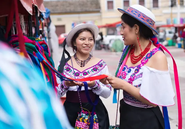 Geleneksel Andean giysileri ve şapkalar giyen iki gülümseyen yerli otavalo ekvadorlu kadın And Dağları 'ndaki bir açık hava pazarında renkli kurdeleler seçiyorlar.