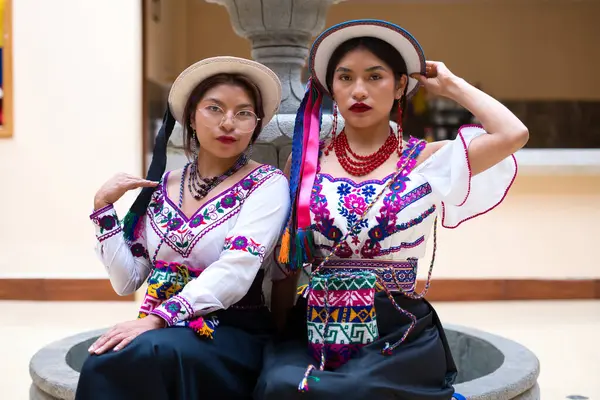 Geleneksel andean işlemeli bluzlar ve renkli şapkalar giyen, riobamba 'dan gülümseyen iki yerli kadın, zengin kültürlerini kutlamak için canlı bir çeşmenin yanında zarif bir şekilde poz veriyorlar.