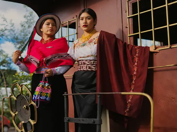 Geleneksel Andean kıyafetleri içinde iki ekvator kadını, canlı renkleri ve kültürel miraslarının karmaşık tasarımlarını vurgulayan eski bir trende poz veriyorlar.
