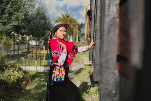 Geleneksel Andean kıyafetleri içinde yerli bir kadın trenin yanında canlı bir şapka takıyor, zengin kültürel mirasını ve eşsiz kıyafetlerini güzel bir şekilde ön plana çıkarıyor.