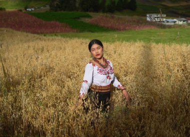 Geleneksel And dekanı kıyafetleri giyen yerli bir kadın buğday tarlasında yürüyor, kültürel mirasını kucaklıyor ve toprakla bağlantısını kuruyor.