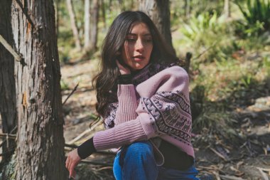 Moda mankeni zarif ve rahat bir süveter ve karmaşık tasarımlar sergiliyor, doğal bir orman ortamında zarifçe poz veriyor, büyüleyici bir moda ve doğa karışımı oluşturuyor.