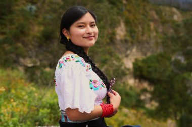 Geleneksel Andean giysileri giyen genç bir kadın canlı bir dağ manzarası arasında huzur içinde gülümsüyor kültürel mirası ve doğal güzelliği gözler önüne seriyor.