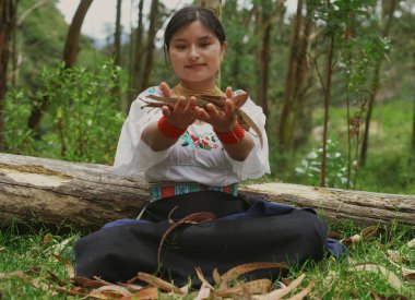 Geleneksel kıyafetlerle süslenmiş yerli bir kadın, gür bir ormanda huzur içinde oturuyor, nazikçe kuru yaprakları tutuyor, doğayla ve kültürel mirasıyla derin bir bağ kuruyor.