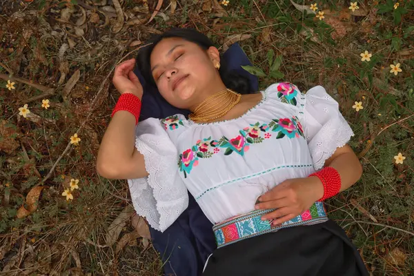 Çiçeklerle çevrili, çimenlerin üzerinde huzur içinde dinlenen genç bir kadın. Kültürel mirası ve doğayla bağlantısını yansıtan rengarenk işlemeli geleneksel giysiler giyiyor.