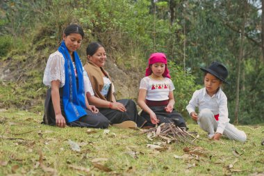 Geleneksel Andean giysileri giyen yerli aile çimlerin üzerinde oturur, ekvatorun pitoresk dağlarında küçük bir şenlik ateşi hazırlar, zengin kültürel miraslarını kutlarlar.