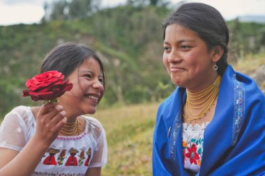 Güzel kırmızı bir gül tutan genç bir kız And Dağları 'nda gülümseyen bir kadınla mutlu bir anı paylaşıyor canlı kültürlerini ve doğanın güzelliğini sergiliyor.