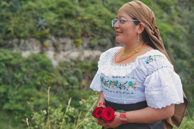 Geleneksel kıyafet ve takılar içinde yerli otavalo bir kadın, Andes dağlarının arka planına karşı iki kırmızı gül tutuyor, kültürel miras ve doğayı somutlaştırıyor.