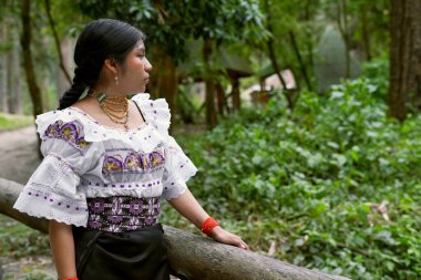 Panama 'da tipik bir ngbe evinin yakınındaki bir ormanda geleneksel nakışlı giysiler ve kolye giyen Ngbebugl kadını, kültürel mirasını gururla gösteriyor.