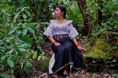 Geleneksel kıyafetler giymiş yerli bir kadın canlı bir ormanda huzur içinde oturuyor. Kültürel mirasını ve etrafındaki doğayla olan güçlü bağını yansıtıyor.